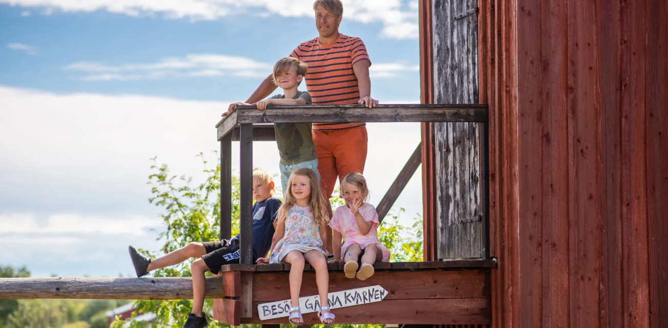 En man och fyra barn vid en röd kvarn på ett somrigt Åland.